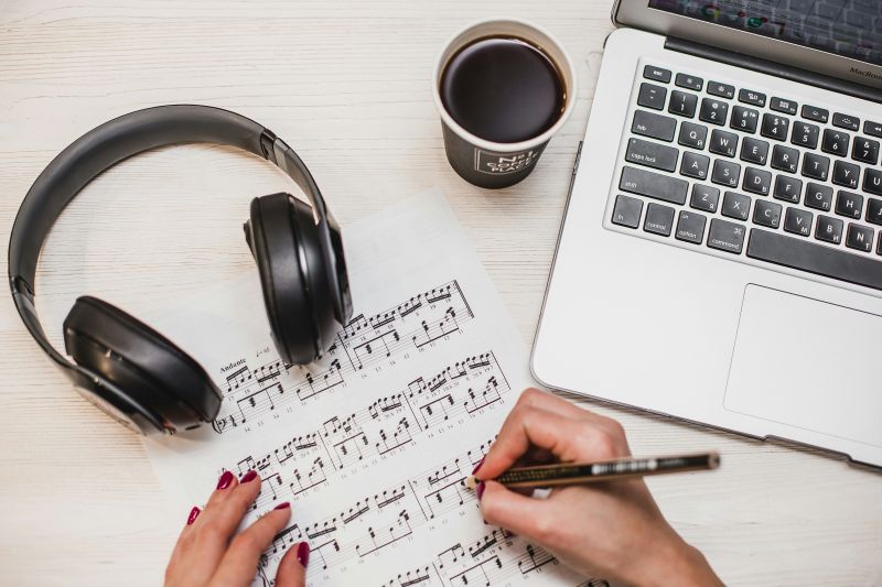 Mac, headset og to hender som noterer på et noteark